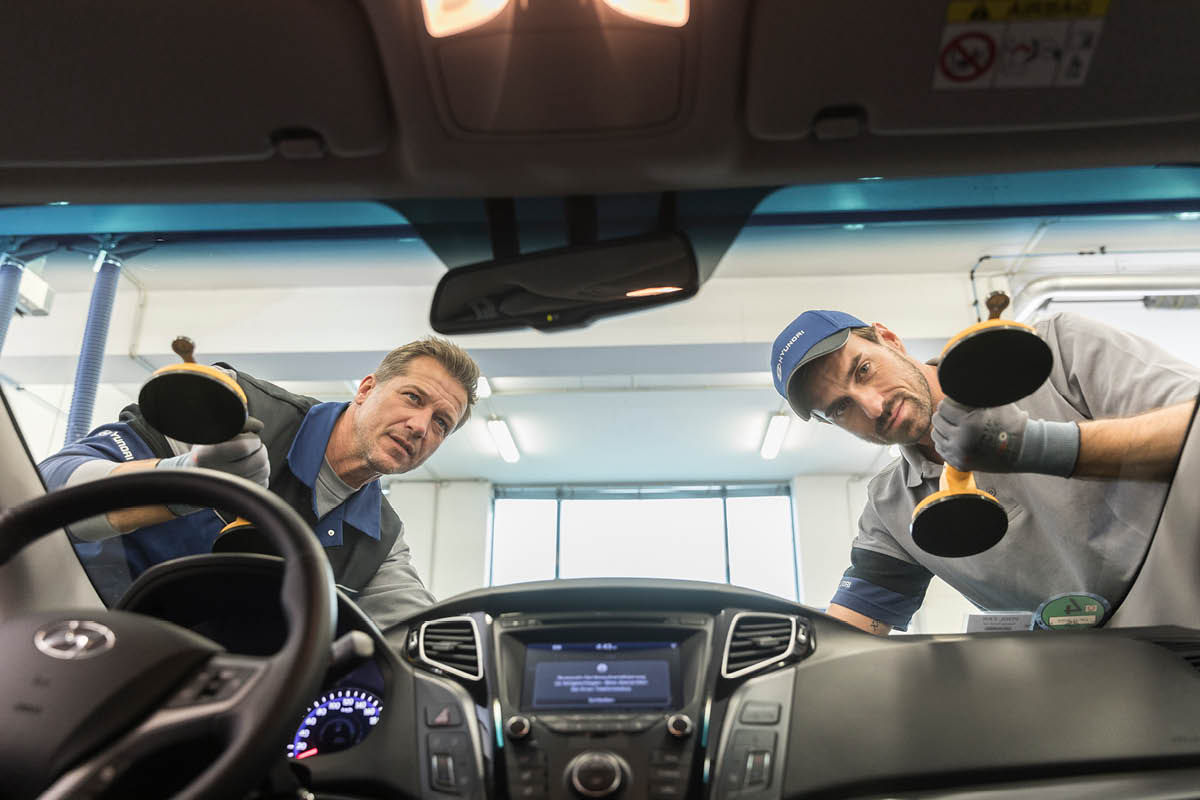 zu sehen sind zwei KFZ Mitarbieter, die eine Autoglassche tauschen