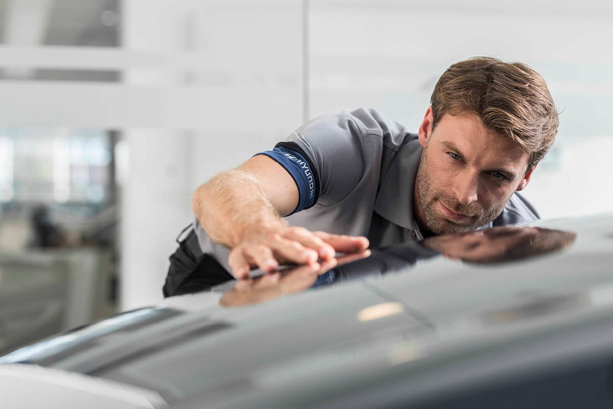 zu sehen ist ein KFZ Mitarbeiter, der ein Auto checkt