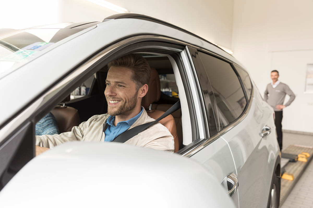 zu sehen ist ein Mann im Auto, der aus der Werkstatt fährt