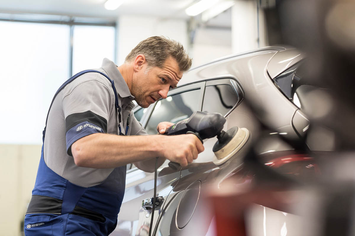 zu sehen ist ein KFZ Mitarbeiter, der ein Auto poliert