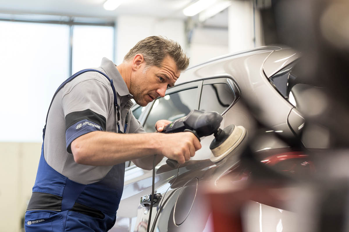 zu sehen ist ein KFZ Mitarbeiter, der ein Auto poliert