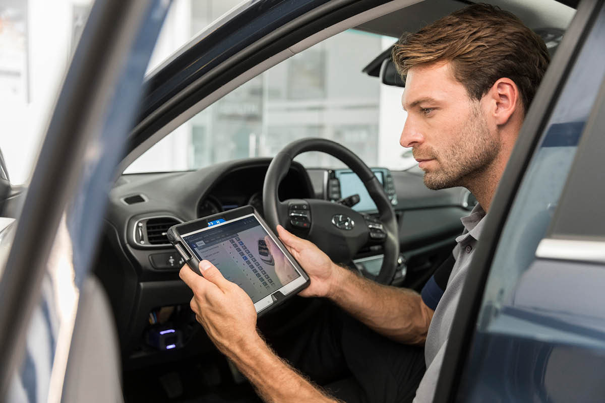 zu sehen ist ein KFZ Mitarbeiter, der in einem Auto sitzt und die Ckeckliste auf seinem Tablet prüft