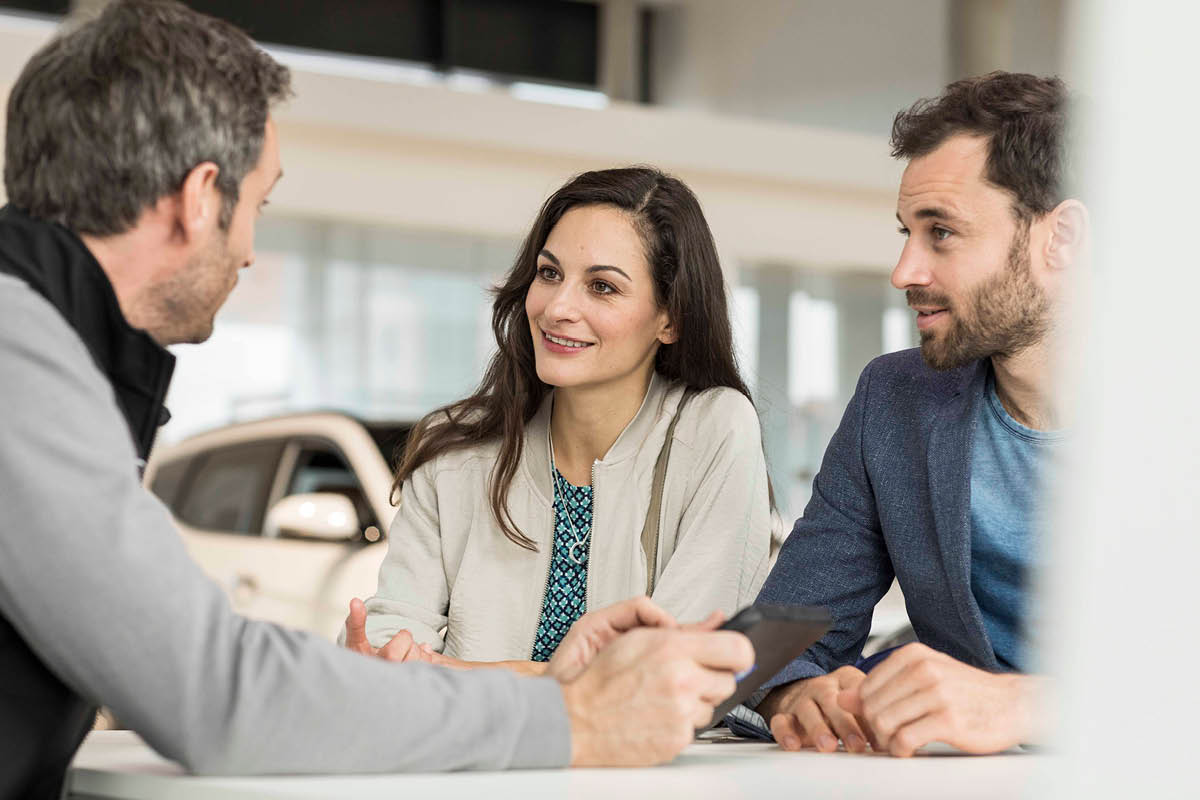 zu sehen ist ein Berater, der ein Paar im Autohaus fachkundig berät