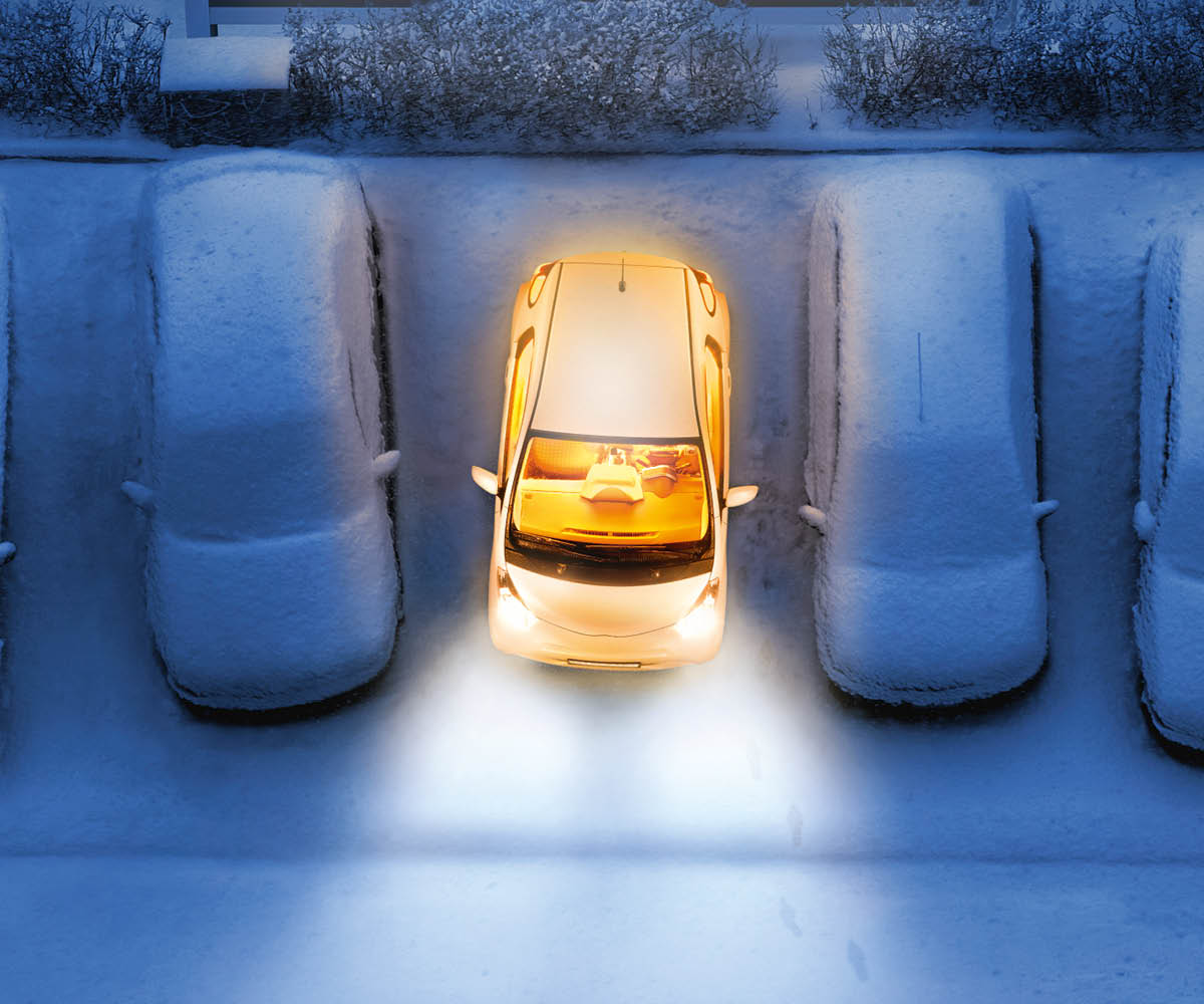 zu sehen ist ein leuchtendes parkendes Auto, daneben stehen verschneite Autos