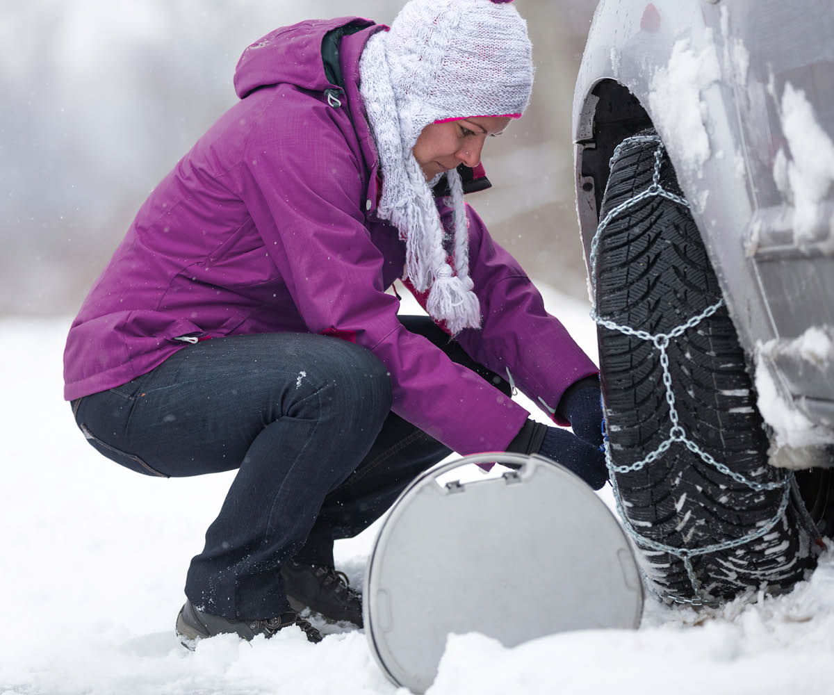 zu sehen ist eine Frau, die Schneeketten wechselt