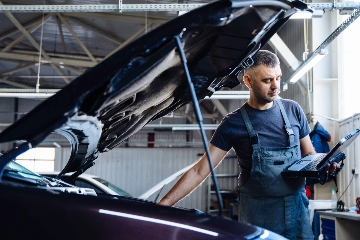 zu sehen ist ein KF Mitarbeiter, der ein Auto im Motorraum prüft